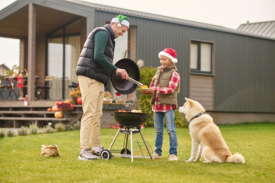 pai servindo filha com churrasco ao ar livre em quintal, com cão ao lado observando