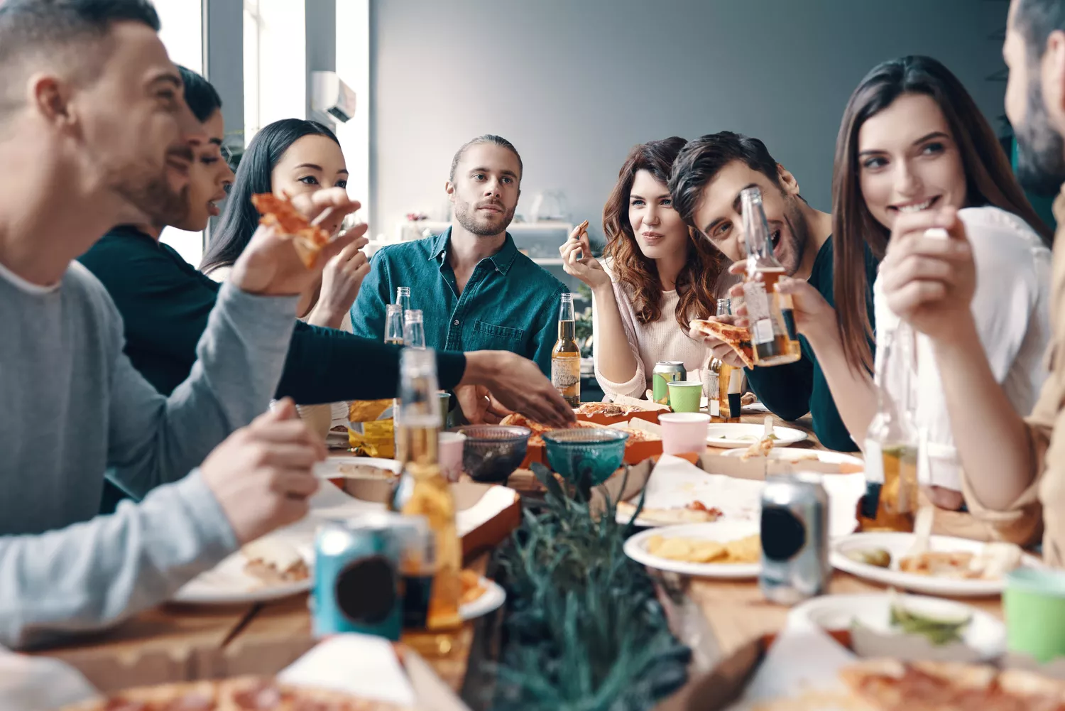 Grupo de pessoas em confraternização ao redor de mesa, com várias bebidas e pratos com entradas