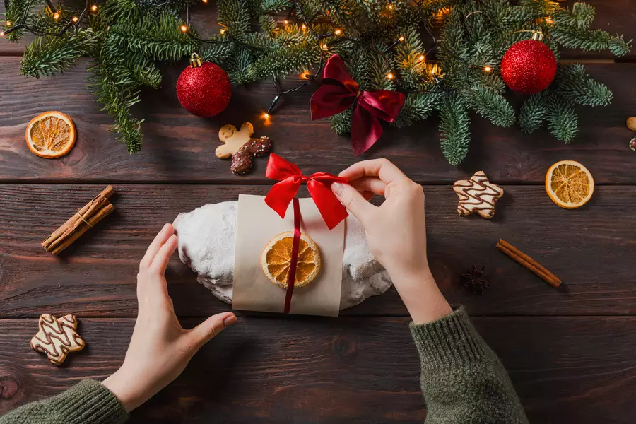 foto de uma mão embrulhando um pacote em frente a uma arvore de natal