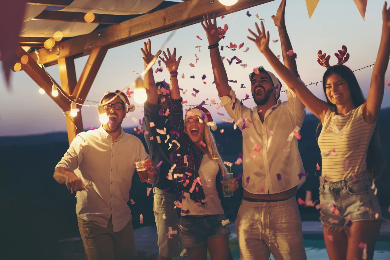 Cinco amigos comemorando juntos com as mãos para o alto e jogando confeti para cima